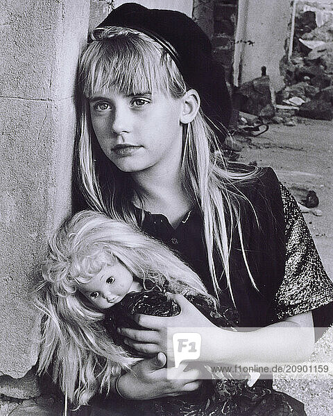 Outdoor portrait of girl child with doll by old building.