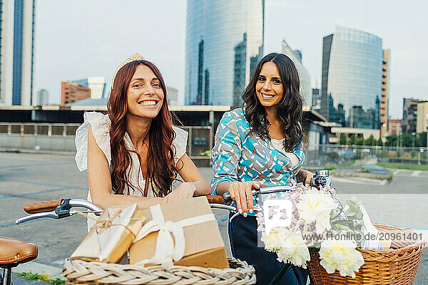 Happy friends standing with bicycles and gifts in front of buildings