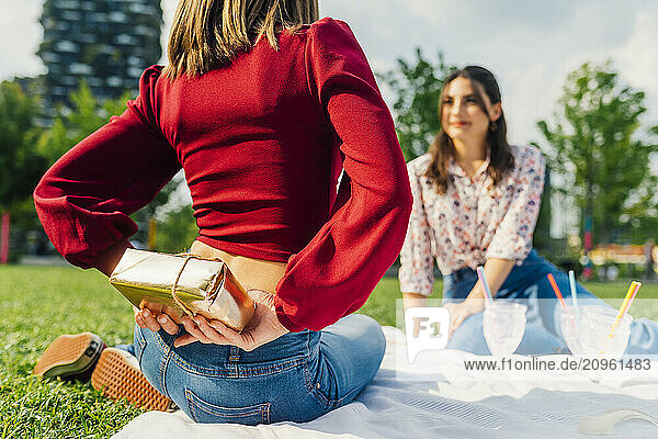 Woman hiding gift box behind back in front of friend