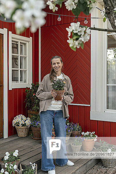Smiling woman holding plant standing on porch