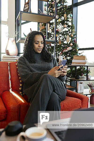 Businesswoman using smart phone sitting on chair at coworking space