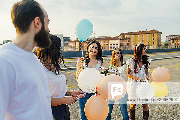 Happy friends standing with balloons on road