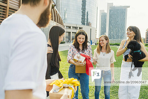 Happy friends giving gifts to woman in park