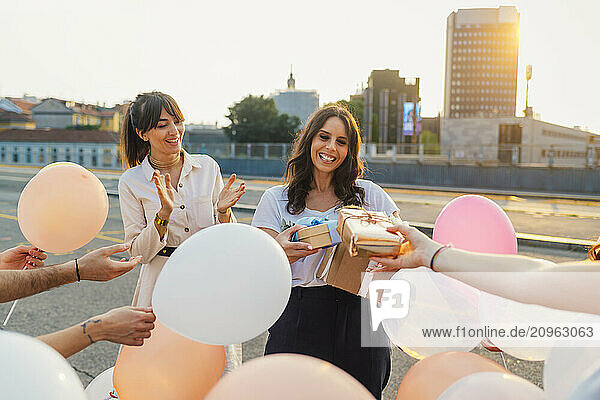 Happy woman taking gifts from friends and celebrating birthday at sunset