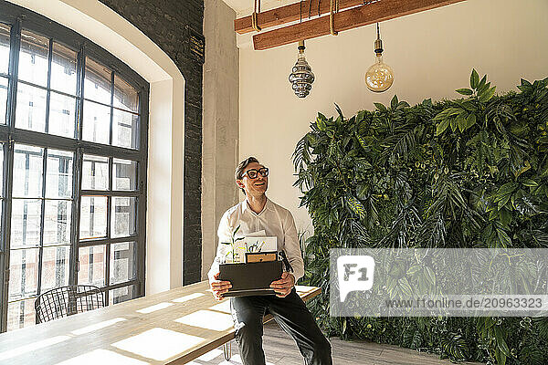 Smiling businessman sitting with belongings on desk