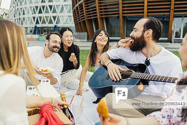 Happy friends together having snacks and enjoying picnic in park