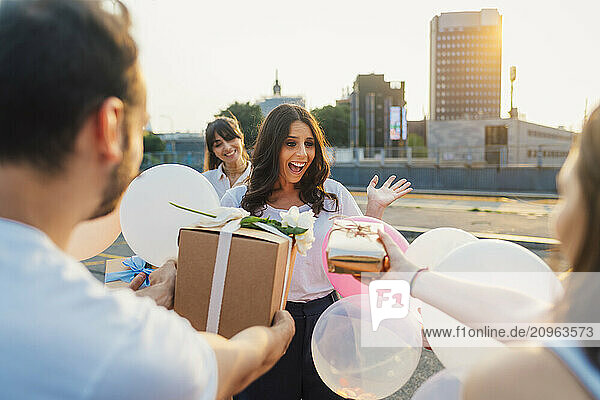 Surprised woman with friends giving gifts and celebrating birthday together