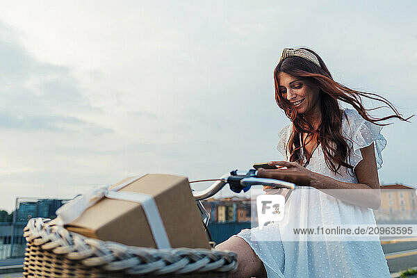 Happy woman using smart phone on bicycle at sunset