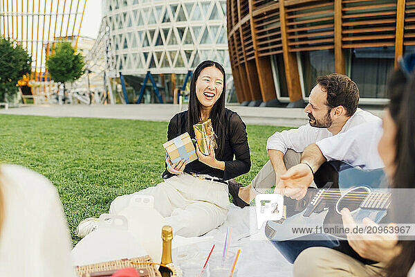 Cheerful woman holding gift boxes with friends sitting in park