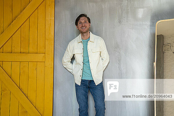 Happy man with hands behind back leaning on gray wall