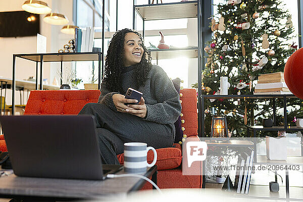 Smiling businesswoman sitting on chair holding smart phone at coworking space