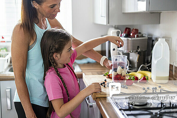 Girl helping mother in preparing milkshake at home