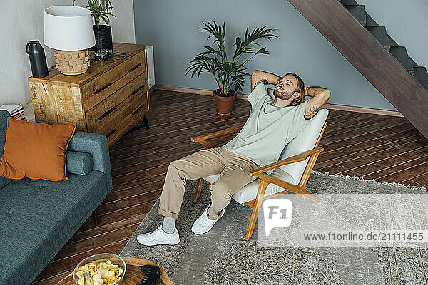 Man with hands behind head relaxing on armchair at home