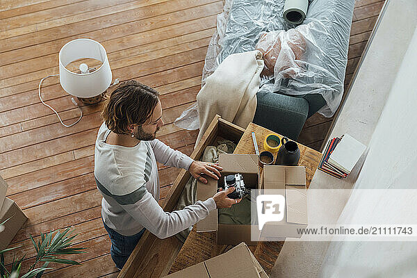 Young man packing camera in cardboard box at home