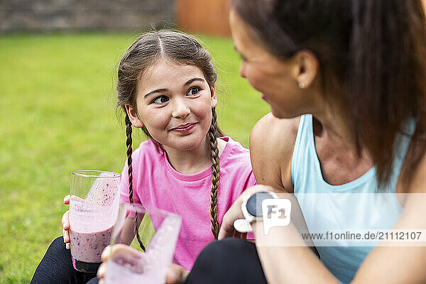Girl with braided hair holding smoothie glass sitting next to mother in back yard
