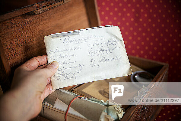 Woman holding a handwritten old letter above an open wooden box filled with memories and family history.