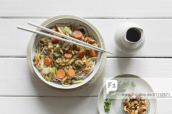 Bowl with fried white cabbage  carrots  spring onions and roasted cashew on rice noodles
