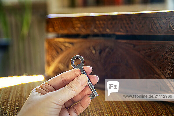 A woman holds an old key in her hand  with a slightly opened wooden box in the background.