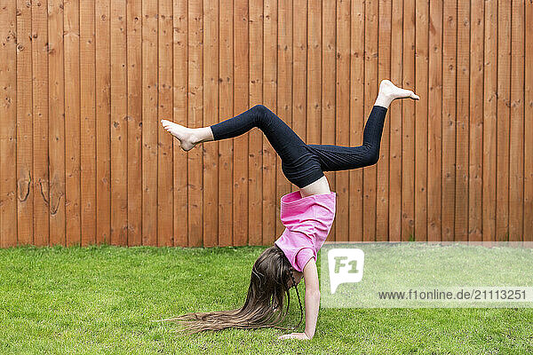 Girl doing handstand on grass in back yard