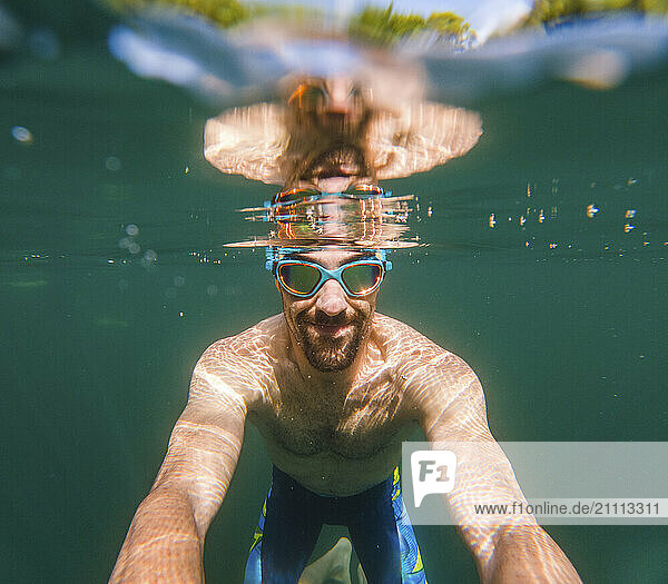 Happy man in swimming goggles taking selfie underwater