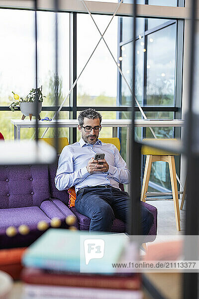 Businessman sitting on sofa and using smart phone at co working space
