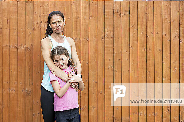 Smiling woman standing with daughter in front of wooden fence