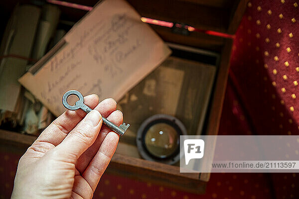 A woman holds an old key over an open wooden box filled with letters and photographs  representing memories and family history.