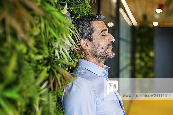 Businessman with eyes closed leaning on wall at co working space