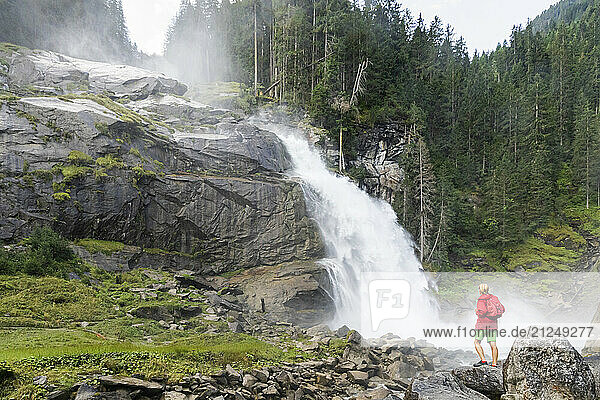 Hiker standing on rocks and looking at the Krimml Waterfalls in Hohe Tauern National Park  Salzburg Province  Austria.
