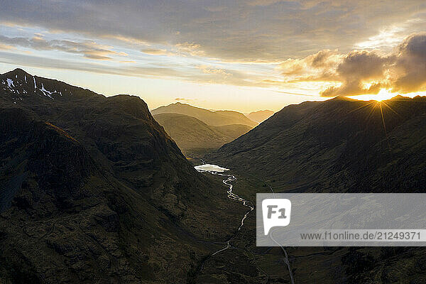 View of Glencoe valley in Scotland with a road through it and mountains on the sides at sunset.