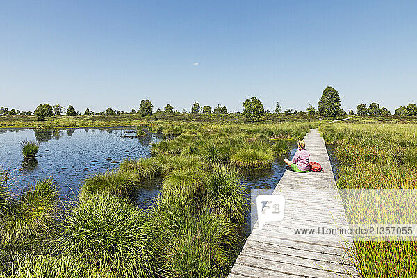 Senior woman sitting on boardwalk under sky in High Fens national park  Wallonia  Belgium