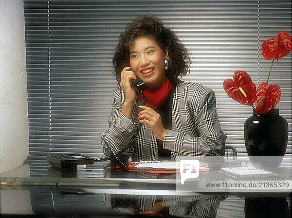 Business woman sitting at office desk using telephone.