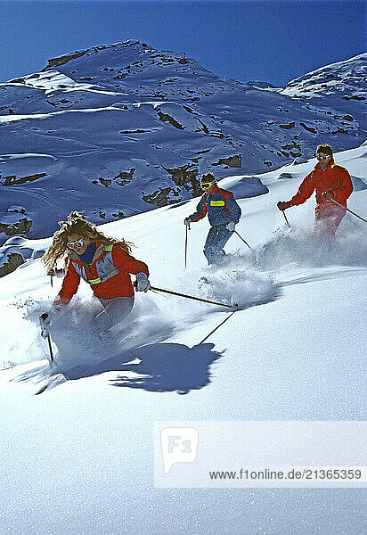 Australia. Young woman & two men downhill skiing in powder snow.