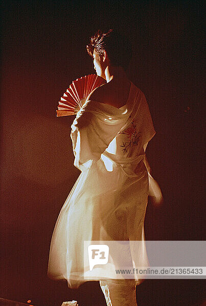 Japanese young man in kimono with hand fan standing in studio.