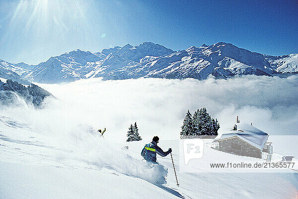 Switzerland. Verbier. Young man skiing. Chalet in background.