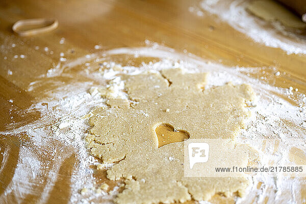 A heart shaped cut-out on a wooden surface covered in flour and cookie dough scraps.