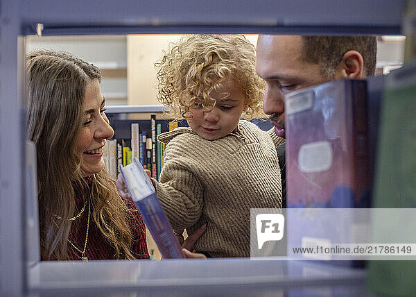 A family enjoys time together browsing books at a library  with a toddler in the arms of a smiling man and an engaged woman by their side. Cleveland  Ohio  USA