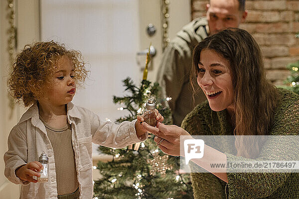 A woman and a young child decorate a Christmas tree while a man watches from the doorway  Ohio  USA