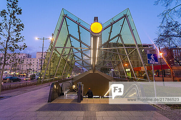 Modern metro station entrance at twilight with illuminated signage and reflective glass structure  Warsaw  Poland