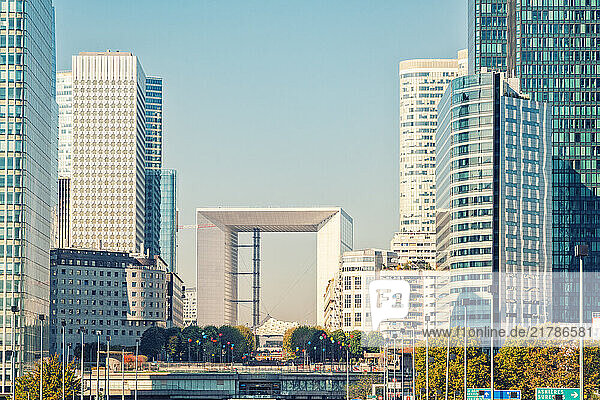 Urban skyline with modern skyscrapers at La Defense with the Arch of La Defense and a busy highway under clear blue skies  Paris  France