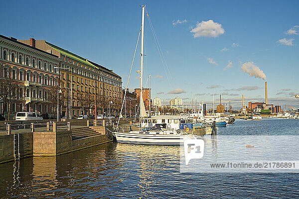 Sailboat moored at Helsinki waterfront on a sunny day with historic buildings and a smokestack in the background  Finland