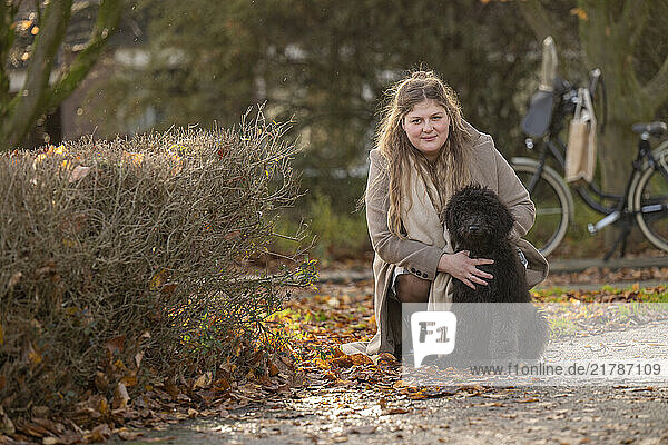 Woman crouching next to a black dog in a park with a bicycle in the background.