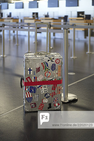 Suitcase with travel stickers in empty airport terminal with check-in counters in background