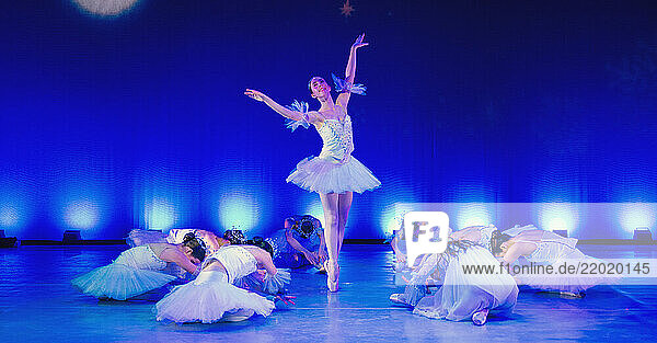 Ballerina performing center stage with dancers gracefully posed around her in a blue-lit theater. The Nutcracker  Bainbridge Island  USA