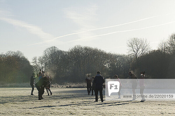 A group of people participates in an outdoor fitness training session on a frosty field  surrounded by trees and a clear sky. Sale Water Park  Manchester  UK