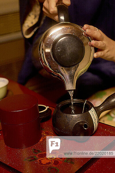 Hands pouring hot water from teapot into a traditional Japanese teacup on a wooden tray  Japanese Alps  Shiba Onsen