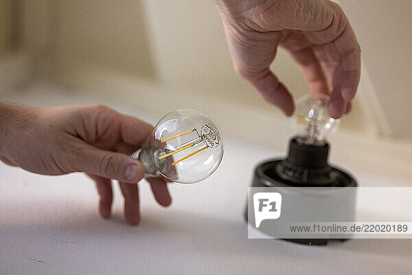Hands installing a new LED light bulb into a black socket on a white surface. Netherlands