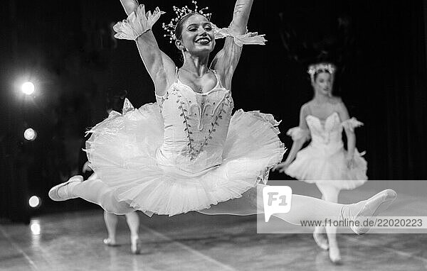 Ballerina performs a graceful leap on stage  wearing a white tutu  with another dancer in the background. The Nutcracker  Bainbridge Island  USA