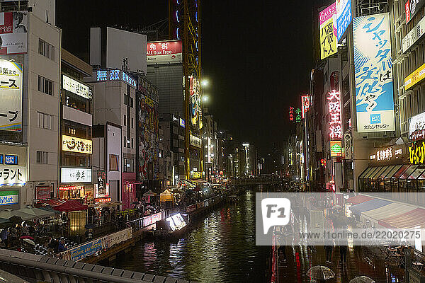 Bustling urban canal scene in Osaka at night with vibrant neon lights illuminating buildings. Osaka  Japan