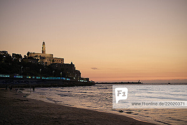 Coastal cityscape at dusk with a prominent lighthouse silhouette against a colorful sky  Israel